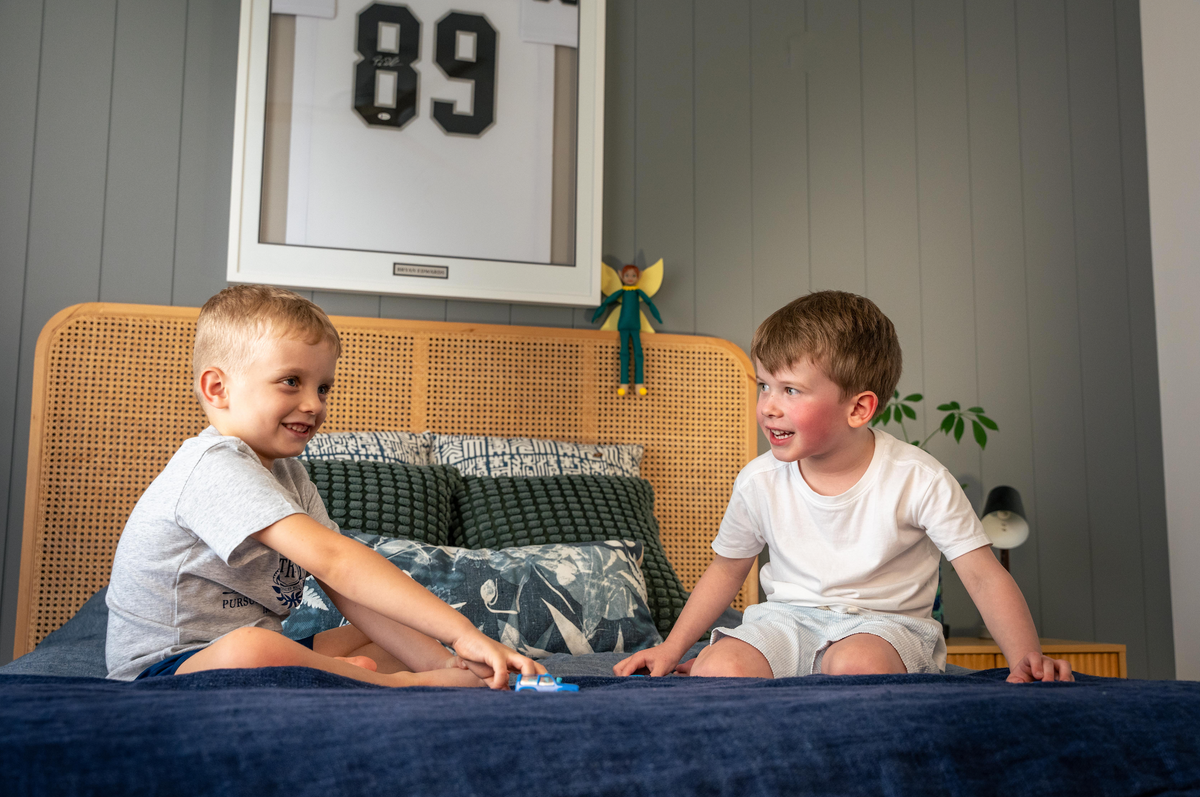 Two brothers sitting on a bed together with a Tooth Pixie doll watching over them in their bedroom