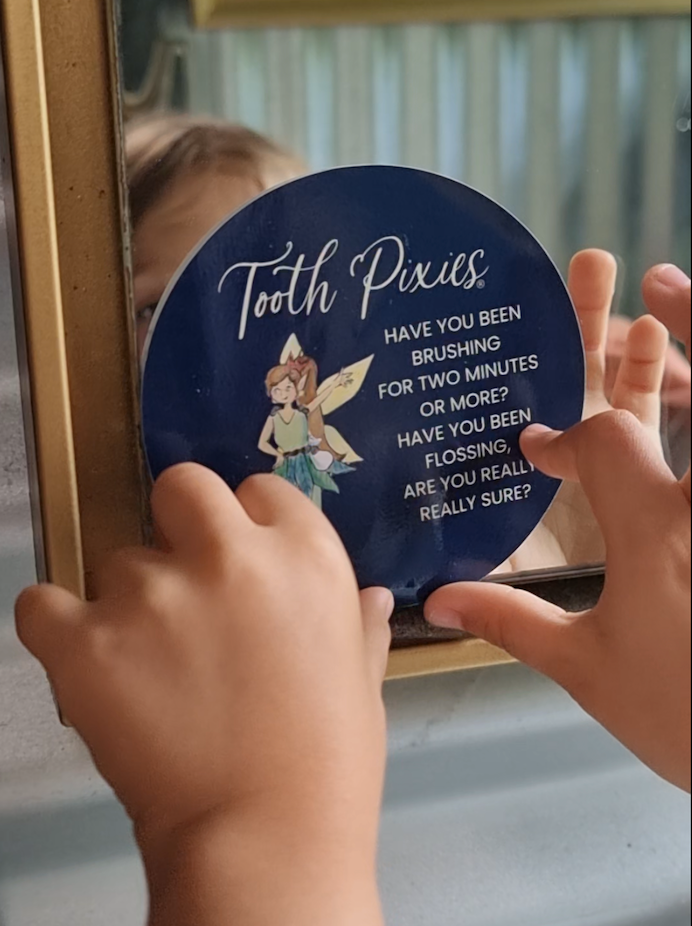Child holding a 'Tooth Pixies' mirror with dental hygiene message
